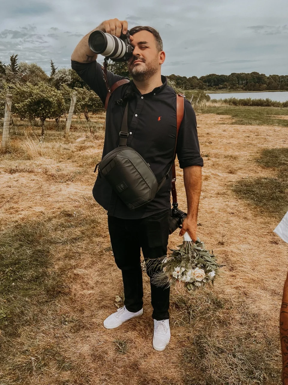 Liam Farrell photographing a wedding, camera raised and bouquet in hand